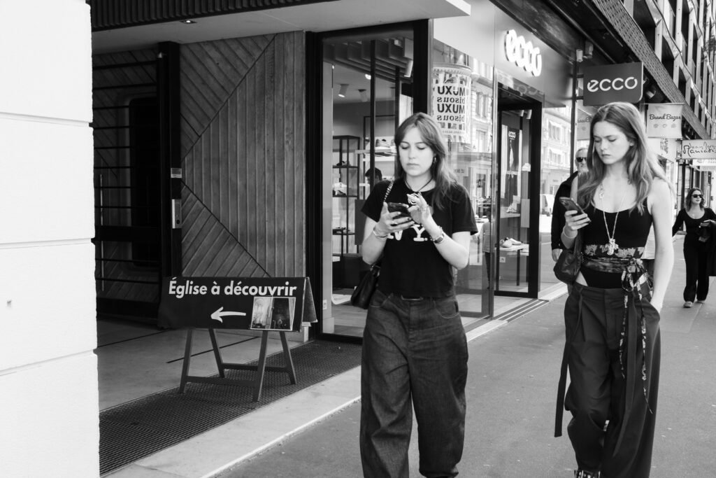 Deux jeunes femmes marchant sur un trottoir, les yeux rivés sur leur téléphone