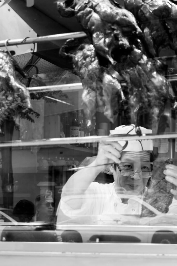 Cuisinier vu à travers une vitrine où pendent des canards laqués