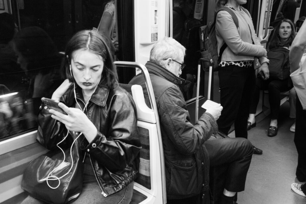 Jeune femme aux écouteurs regardant son téléphone dans une rame de métro, parmi d'autres voyageurs
