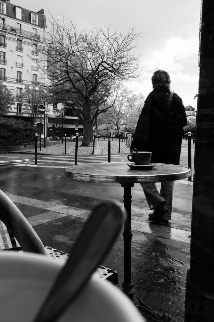 Femme de dos passant devant une table de café avec une tasse, sous la pluie